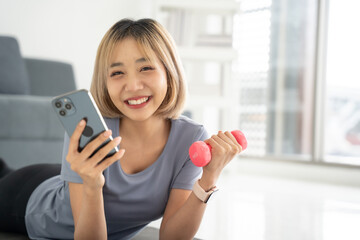 Happy asian woman looking smartphone while exercise in living room at home. Technology and Healthcare concept.