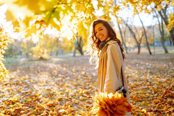 In the autumn park, a happy woman in stylish clothes and a camera is having fun among the fallen...