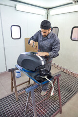 Male mechanic painting motorcycle tank in workshop