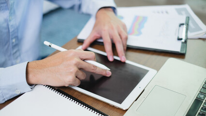 Businessman or manager taps tablet embracing the world of technology and internet focus on finance searching for information online from corporate matters to marketing strategies. In his modern office