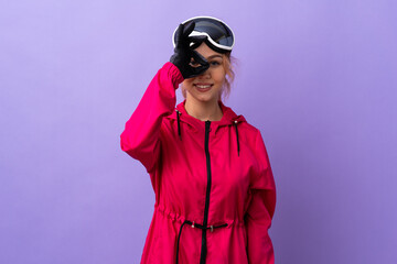 Skier teenager girl with snowboarding glasses over isolated purple background showing ok sign with fingers