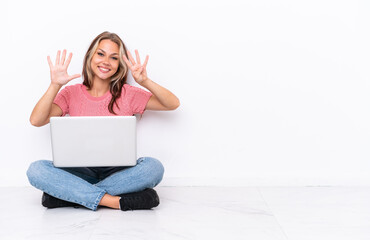 Young Russian girl with a laptop sitting on the floor isolated on white background counting nine...