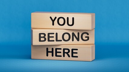 You belong here symbol. Wooden blocks with words You belong here. Businessman hand. Business and You belong here concept. Copy space.3D rendering on blue background.

