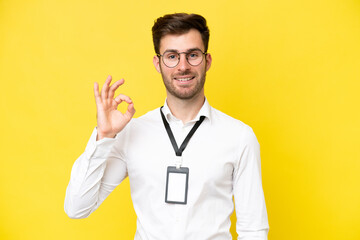 Young caucasian with ID card isolated on yellow background showing ok sign with fingers