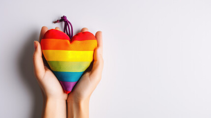 two hands hold a fabric heart in LGBT colors.