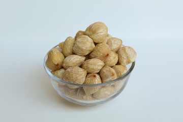 Dried Indonesian Candlenuts, or Kemiri, the seed of Aleurites moluccanus inside a transparant bowl, isolated in white background