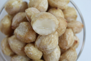 Dried Indonesian Candlenuts, or Kemiri, the seed of Aleurites moluccanus inside a transparant bowl, isolated in white background. Flat lay or top view