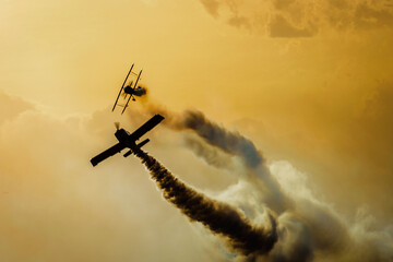 Aviones compitiendo , en una serie dorada , un atardecer a contra luz , mostrando estelas de humo de sus motores , carrera en cielos Mendocinos Arg. - obrazy, fototapety, plakaty