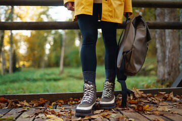 Women's feet in boots go along a wooden walking path in the autumn forest. Vacation travel concept, hiking trail