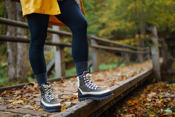 Women's feet in boots go along a wooden walking path in the autumn forest. Vacation travel concept,...