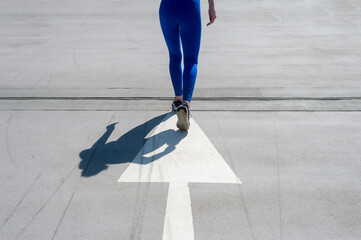 shadow of a woman athlete jogger in road, running over a painted arrow