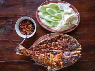 Grilled giant trevally or ikan kue bakar with red barbeque and chili sauce on a plate. Served with...