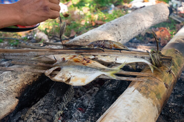 Grilling fresh fish on bamboo skewers with sweet soy sauce (kecap manis) as seasoning on the beach. A simple and traditional way.