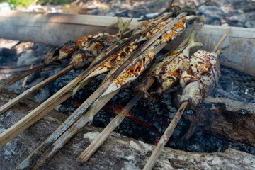 Fototapeta na wymiar Grilling fresh fish on bamboo skewers with sweet soy sauce (kecap manis) as seasoning on the beach. A simple and traditional way.