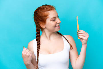 Obraz premium Young caucasian reddish woman brushing teeth isolated on blue background celebrating a victory