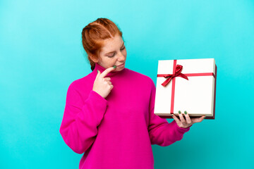 Young caucasian reddish woman holding a gift isolated on blue background with sad expression