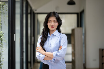 Smart and self-confident businesswoman standing with arms crossed at desk in office