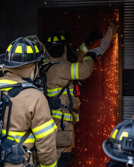 firefights use an electric saw to cut through the door of a building during a training exercise. 