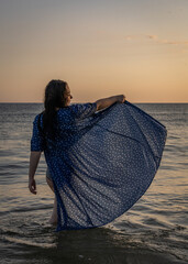 kobieta stojąca w morzu z uniesiona sukienką - obrazy, fototapety, plakaty