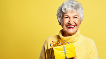 Happy smiling senior woman holding gift box over yellow background