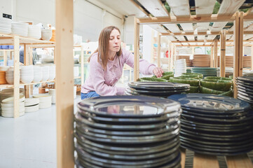 Shopping in a pottery store. Young woman looking for ceramic tableware and utensils in a craft shop.