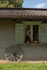 Picturesque garden shed or small cottage with old variate wheel leaning against the wall and window shutters open
