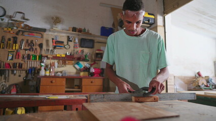 One Focused Black Brazilian Carpenter sawing Wood in Workshop. Young apprentice working at carpentry business