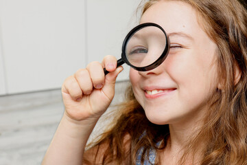 portrait of a cute smiling girl looking through a magnifying glass