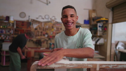 One young black carpenter polishing wooden furniture standing inside carpentry workshop. Concentrated worker repairing and creating handmade object