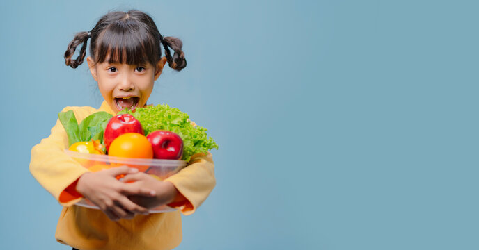 A little girl is holding a bowl of fruits and vegetables.
