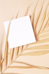 Greeting card mockup and dried palm leaf on beige background top view flatlay. Card mock-up with copy space.
