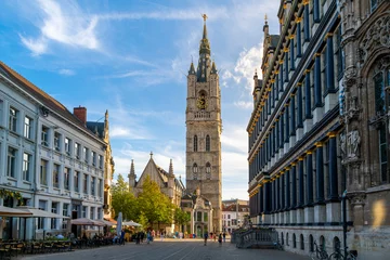 Photo sur Plexiglas Europe du nord Sunlight shines on the medieval Ghent Belfry tower, or Het Belfort van Gent, with City Hall on the right and sidewalk cafes on the left, in the historic old town of Ghent, Belgium.