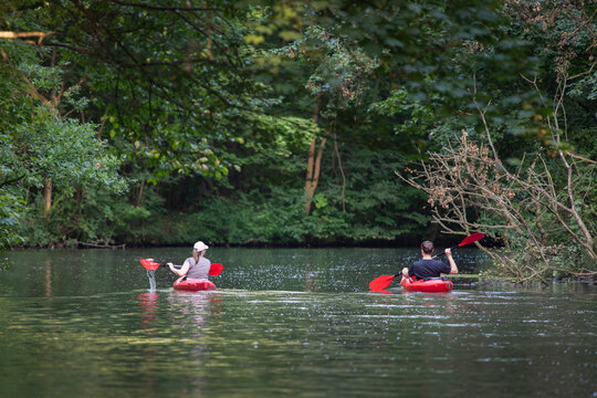 A couple swims on two red caiques along a forest river. Healthy outdoor activities.