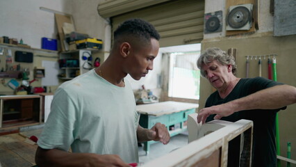 Obraz premium Carpenters working at workshop. Senior and young employee polishing wooden furniture, authentic Brazilian small business in South America