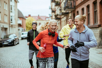 Young group of friends running and jogging together in the city during winter or autumn