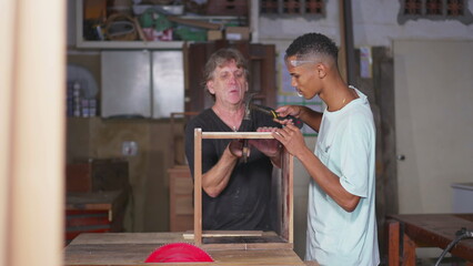 Master Carpenter Mentoring Young Apprentice in Furniture Craftsmanship at Workshop