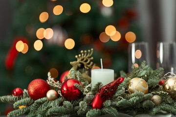 a composition with a candle, red and gold ornaments. Christmas and New Year's concept, interior details, selective accent on the background of a fir tree with a bokeh effect