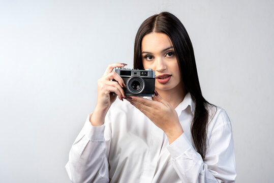 young latin woman holding an old photo camera dressed in white shirt and white background