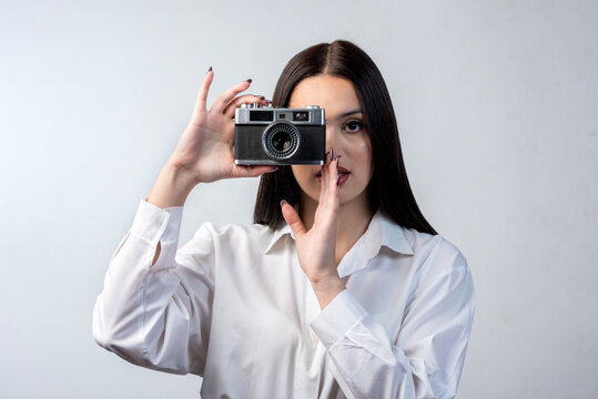 young latin woman holding an old photo camera dressed in white shirt and white background