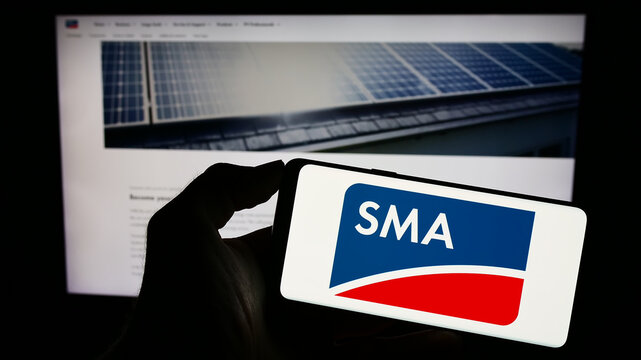 Stuttgart, Germany - 08-21-2023: Person holding smartphone with logo of German company SMA Solar Technology AG on screen in front of website. Focus on phone display.