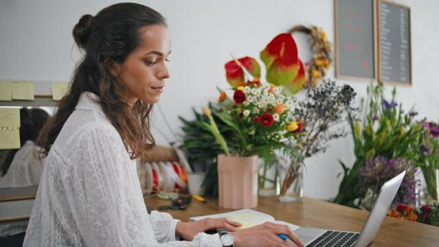 Serious florist work laptop digital device in flowers store. Focused woman work.