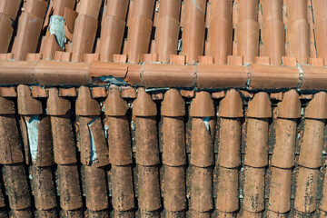 Close-up of damaged roof tiles, some broken and missing, revealing the underlying structure. A concept image for roofing problems and maintenance.