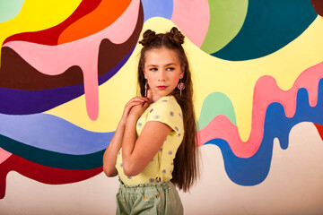 Portrait of adorable pondering cover kid girl in yellow t-shirt posing at colorful wall, pensive looking away. Thoughtful child poses in studio indoors. Summer fashion concept. Copy ad text space