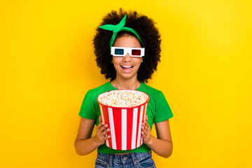 Photo of funky cheerful girl toothy smile hands hold big popcorn box watch movie 3d glasses isolated on yellow color background