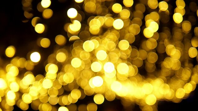 A close-up of a garland with golden lights hanging in the park in the evening, a blurry image. Bokeh.