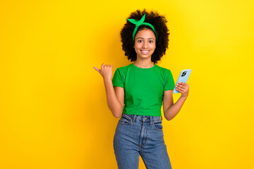 Photo of beautiful teen schoolgirl hold smart phone indicate finger empty space ad isolated on yellow color background