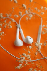 headphones in flowers, white headphones, orange background, listening to music in headphones, relaxation