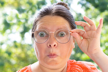 close up female face, funny woman in glasses looks through lenses in surprise, concept unexpected...