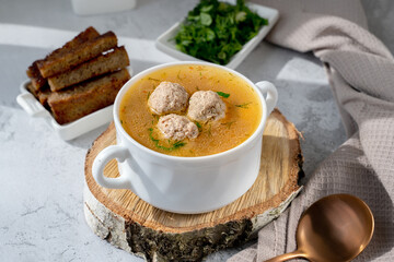 Vegetable soup with meatballs in a white soup cup. Low-calorie soup with herbs and crackers