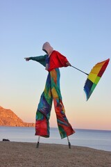 An unusual photo of a man in a colorful rainbow suit walking along the seashore. A man in carnival...